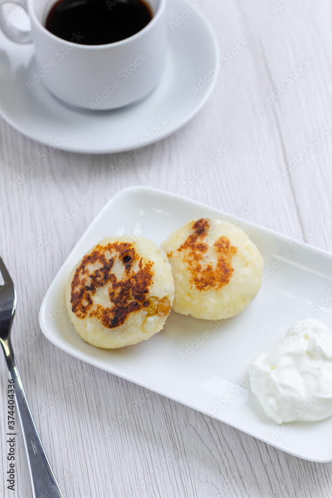 Dessert with cup of coffee on background. Cheese dessert on white plate on white wood table. Delicious breakfast in cafe. Home made bakery. Dessert with cup of coffee on background. Cheese dessert on white plate on white wood table. Delicious breakfast in cafe. Home made bakery.