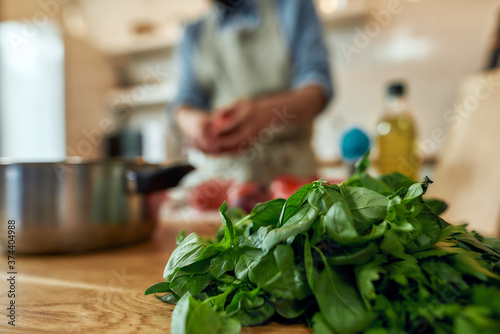 Close up of basil lying on the table. Young man cook preparing healthy meal with vegetables in the background. Italian cuisine concept
