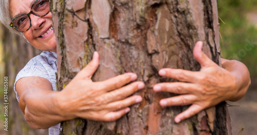 Blurry human hands hugging a tree trunk in the woods - love of the outdoors and nature - earth day concept. An old woman hiding behind the trunk. People save the planet from deforestation
