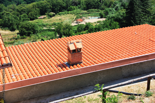 roof with many small identical red tiles in a row and an orange brick chimney in the Tuscan countryside