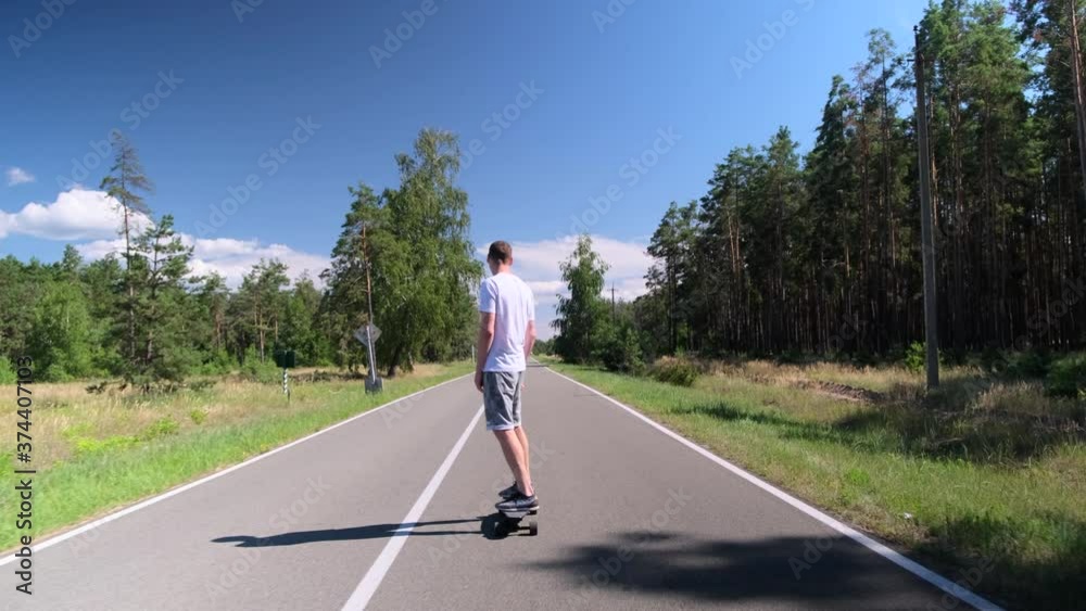 Young adult sports man skateboards on the road in the middle of a pine forest