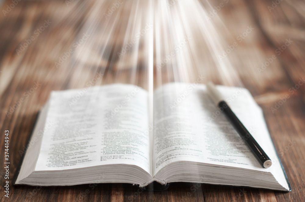 Open Bible book on a wooden table. Light over the book. Open Bible book on a wooden table. Light over the book.