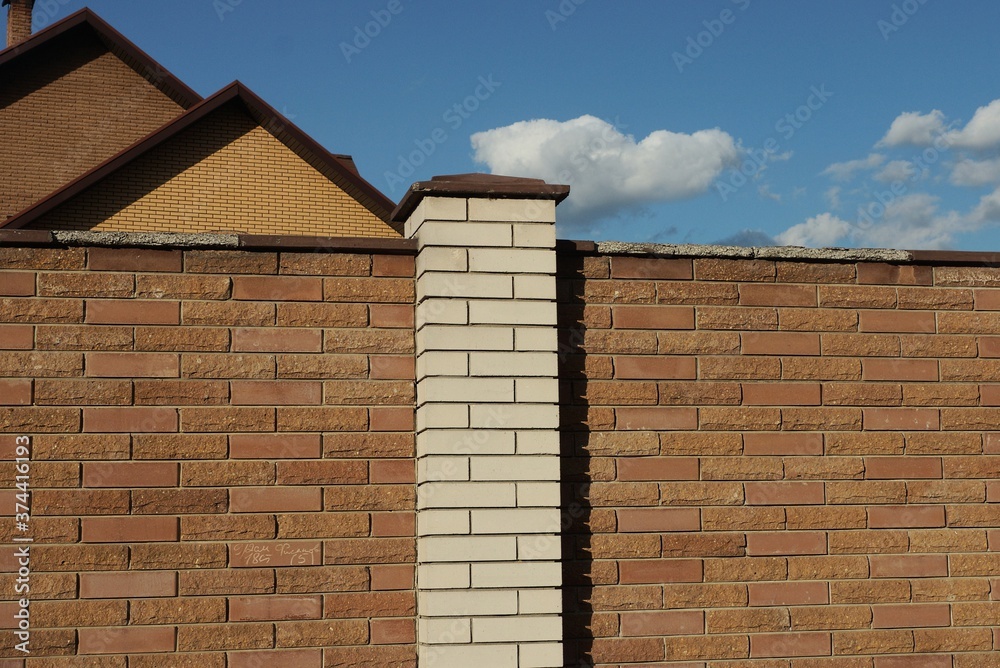 Fototapeta premium part of a wall of a fence made of white and brown bricks on the street against a blue sky