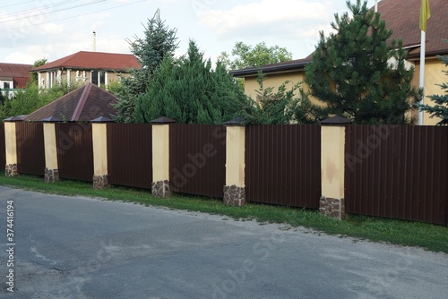 a long brown metal fence with yellow concrete pillars outside by a gray asphalt road