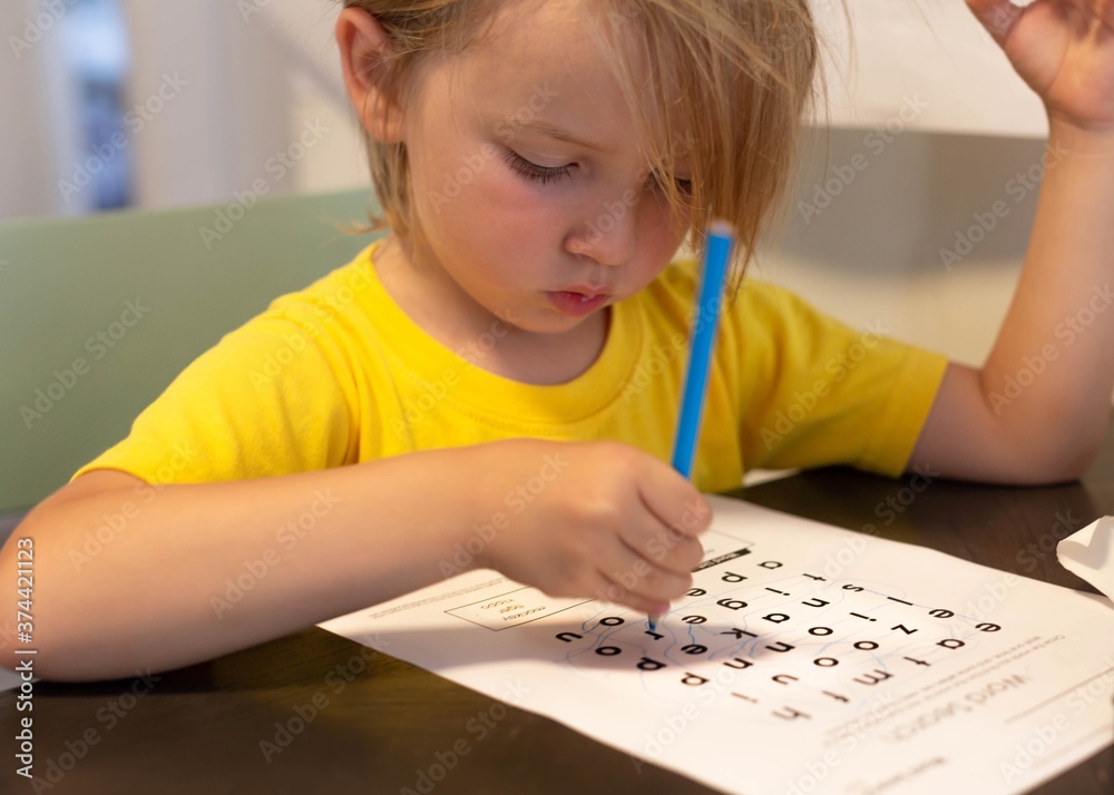 Naklejka premium A young kid doing school work at home. Learning words.