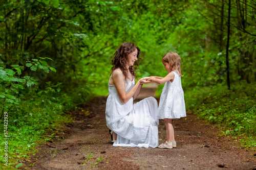 Young Caucasian Mother and Her Daughter Happily Playing Together Outdoors in Green Summer Forest.
