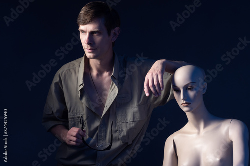Portrait of man next to a mannequin. Man with glasses in his hands on a dark background. Man next to a humanoid cyborg. Human-like cyborg.as a symbol of artificial intelligence. Human leans on cyborg