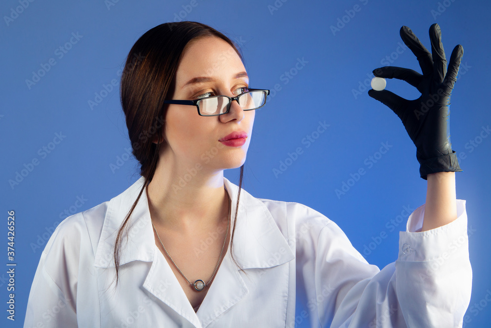 Woman doctor holding a large tablets. Medic shows some kind of pill. Doctor on blue background. Concept is medicine for forestry. She recommends treatment with this medication. Human treatment. Woman doctor holding a large tablets. Medic shows some kind of pill. Doctor on blue background. Concept is medicine for forestry. She recommends treatment with this medication. Human treatment.