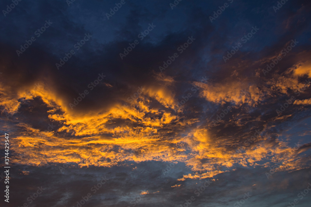Dramatic golden sunset sky. Сlouds are illuminated from below by golden rays of the sun.