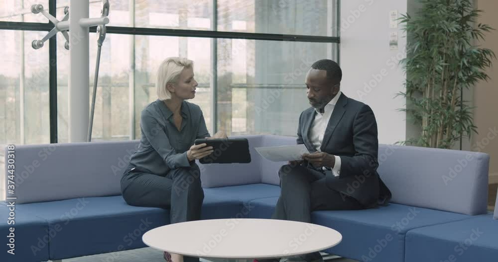 Business people in office meeting in modern lobby on sofa using digital tablet technology for presentation Business people in office meeting in modern lobby on sofa using digital tablet technology for presentation