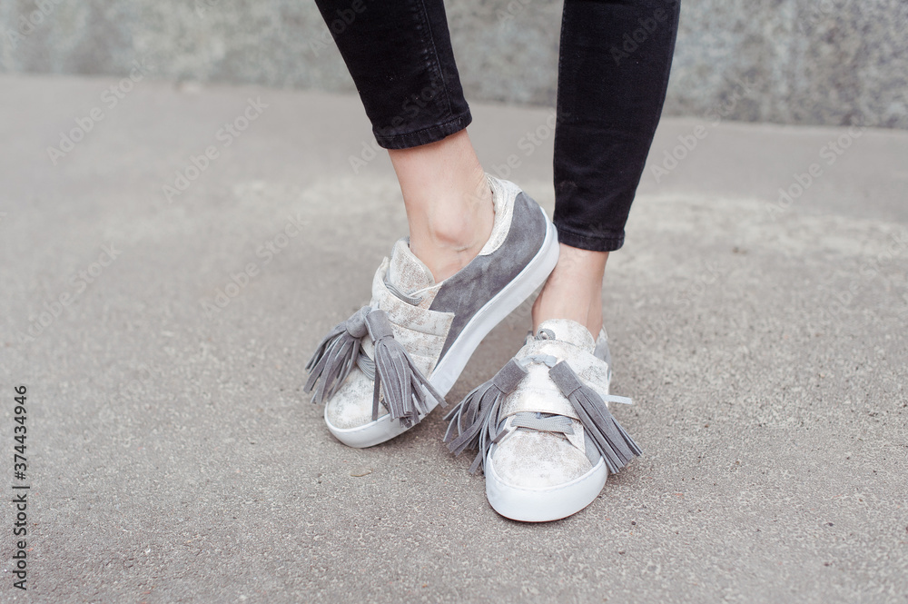 Fashionable young woman wearing black jeans and trendy gray suede sneakers. Street style. Outdoor. 