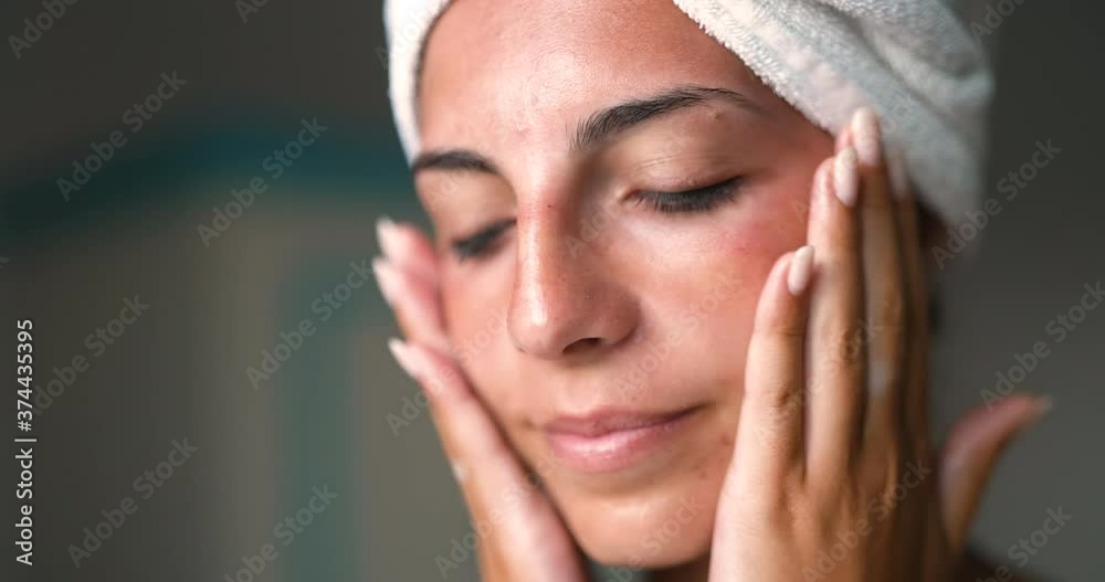 Close up shot of an young smiling woman with perfect skin just cleaned from impurities is gently applying on face with fingers day or night cream in a bathroom. Close up shot of an young smiling woman with perfect skin just cleaned from impurities is gently applying on face with fingers day or night cream in a bathroom.
