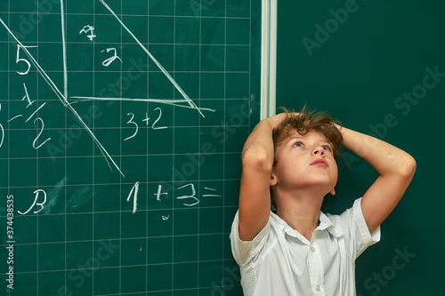 Portrait of a thoughtful boy student at the blackboard . Primary education