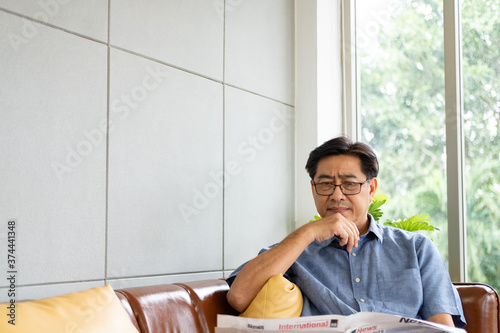 Elder Asian men feeling stress while look or reading at the newspaper in the morning. Eyesight or vision problem in senior people. Emotional depress and feel uncomfortable. with copy space. photo