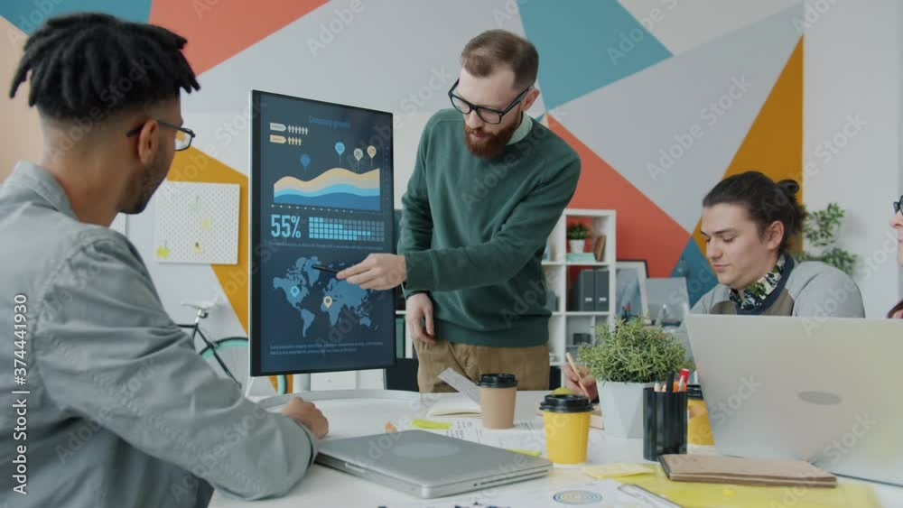 Young man is making presentation using digital screen talking to group of colleagues in office. Modern technology and creative business concept.