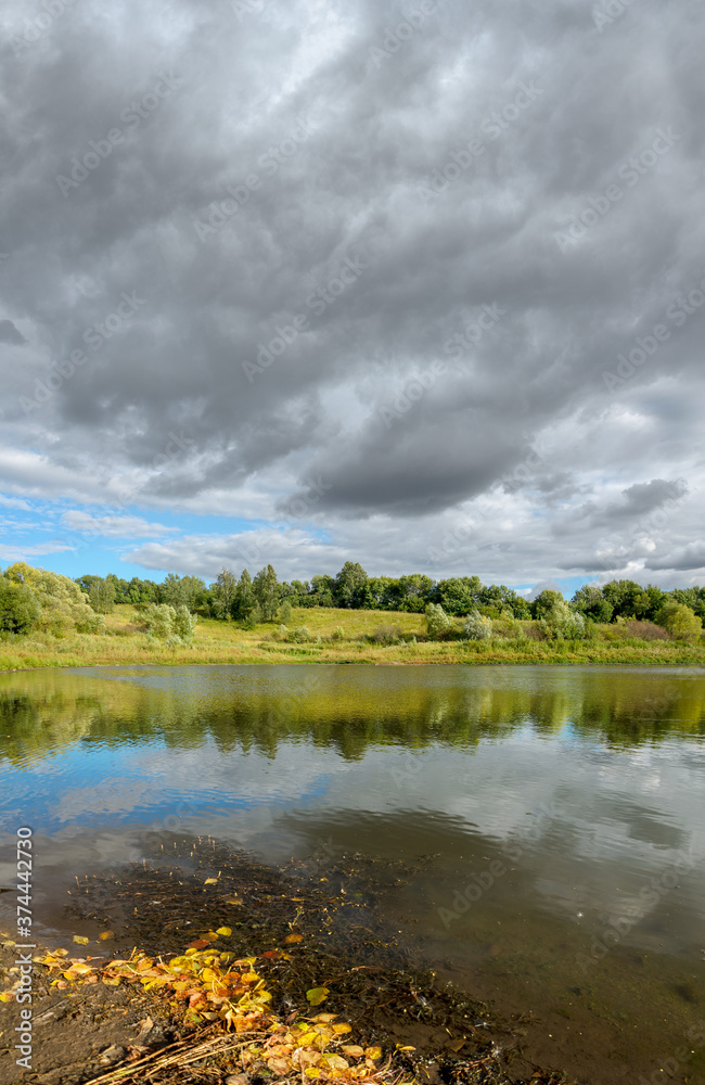 Sunny landscape with calm lake and grey clouds during sunset