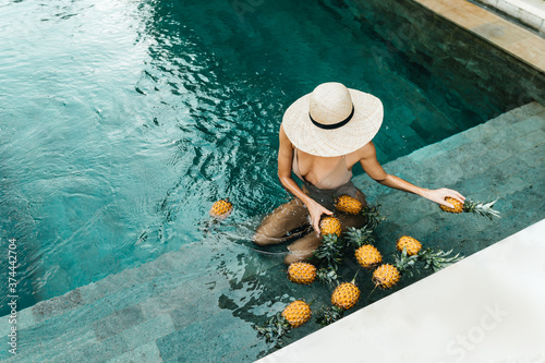 Beauty, Health Concept. Fresh Organic Fruits In Refreshing Pure Water. Beautiful Vegan Woman Relaxing In Swimming Pool With Pineapples. Healthy Lifestyle, Nutrition, Diet. Summer Vacation