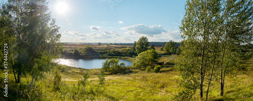 Sunny rural landscape with lake and farm fields 