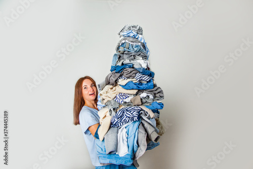 Surprised young red-haired woman carrying pile of cluttered clothes at home. photo