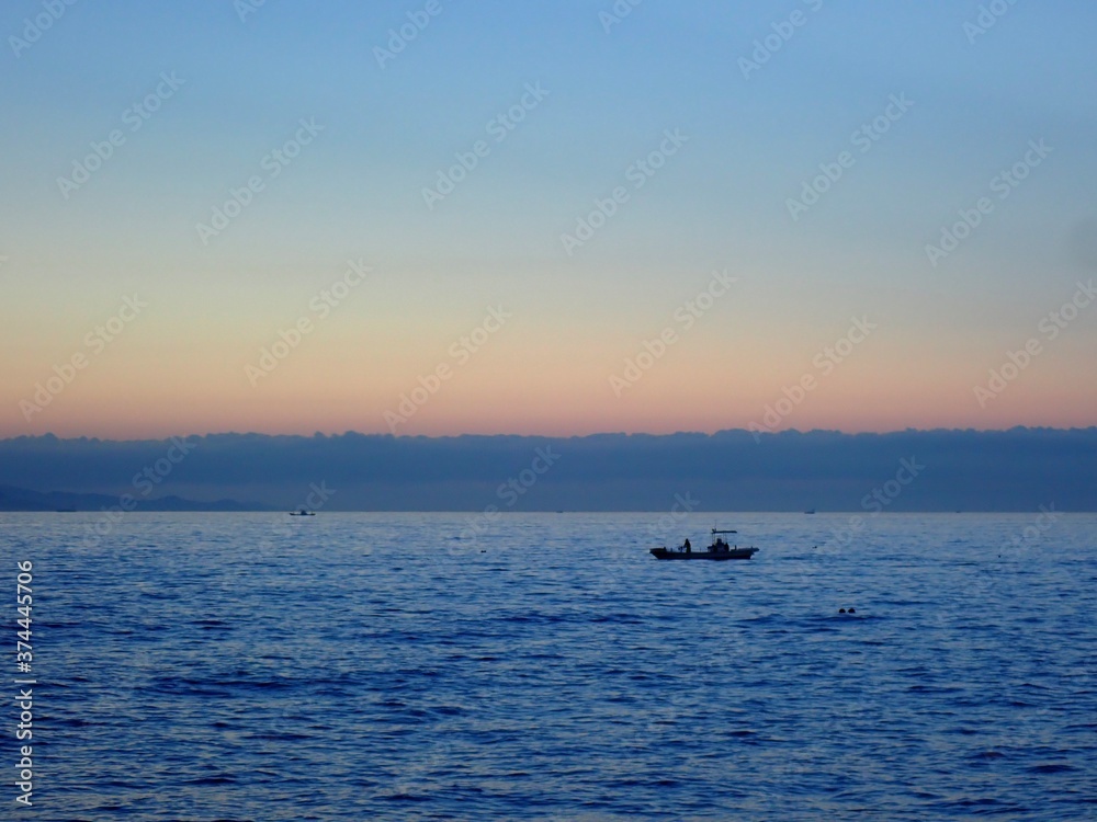夜明けのグラデーションになった空のもと穏やかな海に浮かぶ釣り船