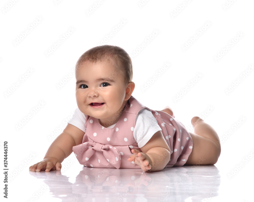 Focused infant baby girl toddler in polka dot dress is lying on stomach holding arm outstretched going to get something Focused infant baby girl toddler in polka dot dress is lying on stomach holding arm outstretched going to get something