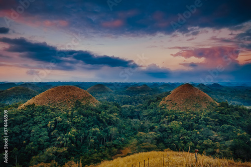 Chocolate Hills, Philippine attraction mountains with green rainforest at sunrise sky. Burnt brown, yellow, orange grass on tops of mounts. Asia greenery landmark in National Park at Bohol Island