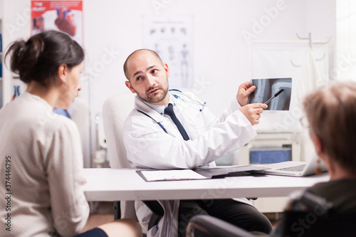 Wallpaper Mural Doctor showing knee injury on x-ray image in hospital office to young woman and her disabled mother in wheelchair. Medic wearing white coat and stethoscope. Torontodigital.ca