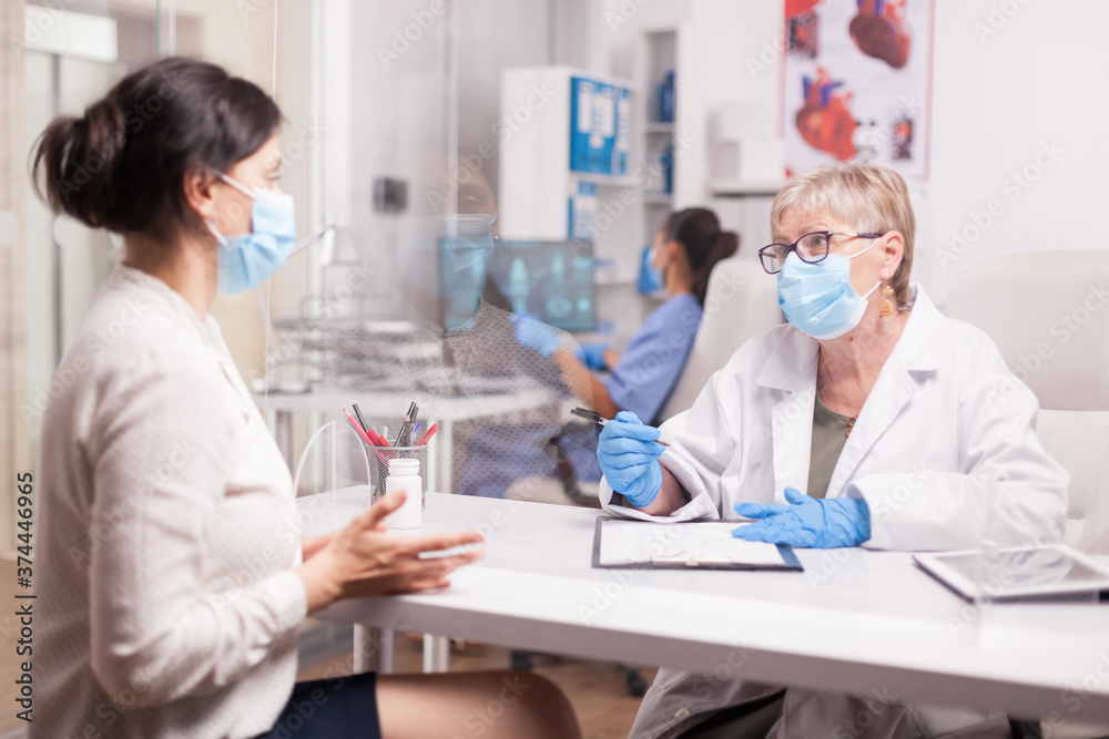 Mature doctor with face mask against coronavirus during consultation with sick young woman in hospital office. Mature doctor with face mask against coronavirus during consultation with sick young woman in hospital office.