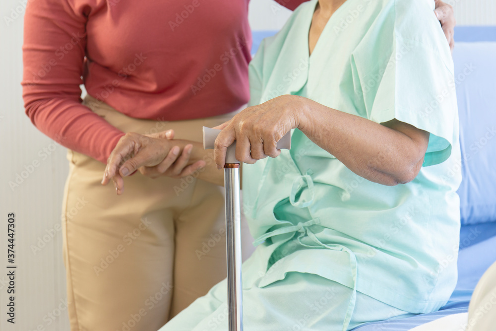 The patient's hand holding the walker helps to stand. There is a woman to take care of and support to stand.