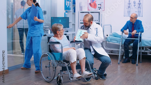 Doctor showing the osteoporosis risk for elderly persons to a senior woman in wheelchair in a rehabilitation clinic, center or hospital. Old man with walking frame, health care medical facility
