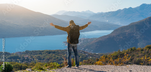 A traveler with a backpack stands on the top of the mountain and holds his hands to the sides 