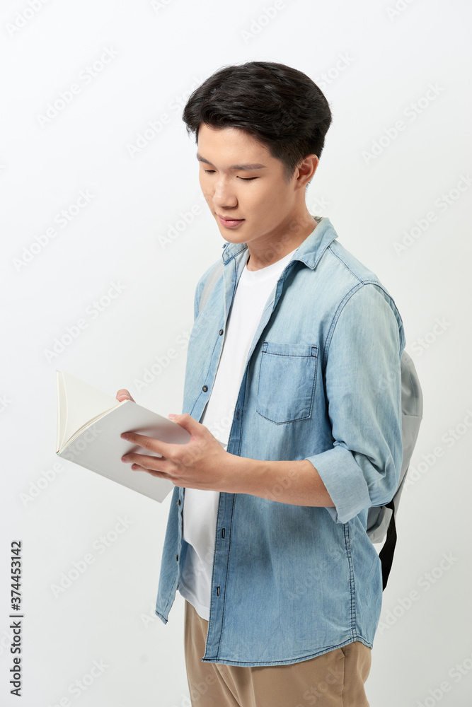 Young Asian man reading book and wearing casual clothing with backpack over white background. Young Asian man reading book and wearing casual clothing with backpack over white background.