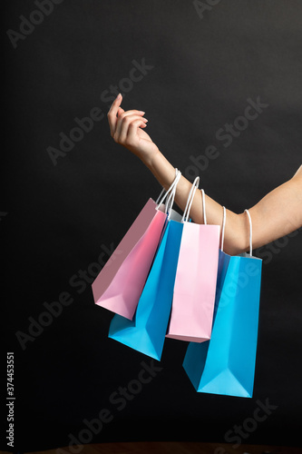 Holiday sale. Black Friday. Blue pink shopping bags hanging on female arm isolated on dark copy space background. Fashion consumerism. Special offer.