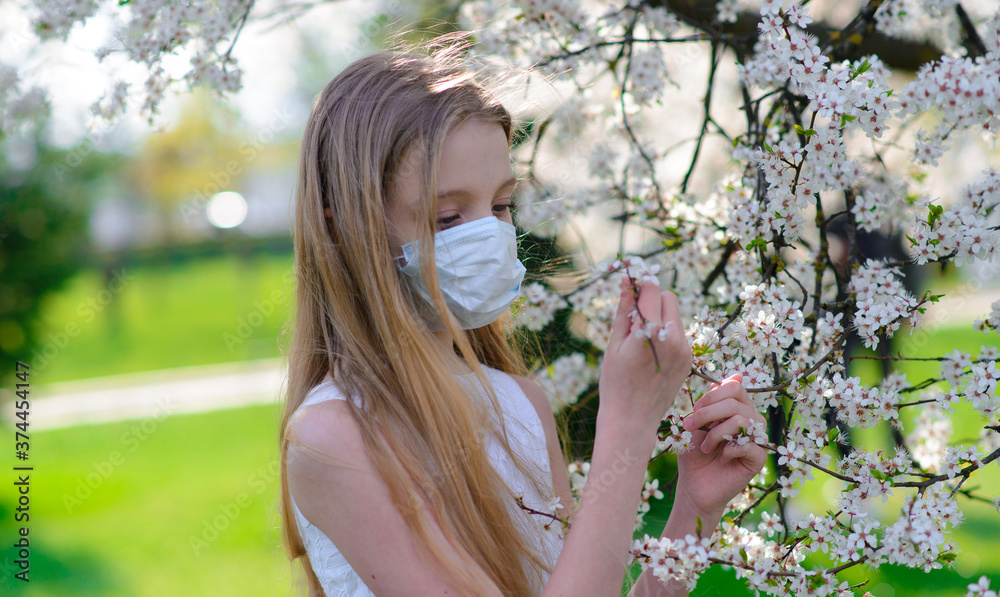 Girl teenager in protective medical mask in the spring among blooming garden. Quarantine coronavirus in Europe. Allergy to flowering trees