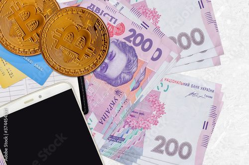 200 Ukrainian hryvnias bills and golden bitcoins with smartphone and credit cards. Cryptocurrency investment concept. Crypto mining or trading photo