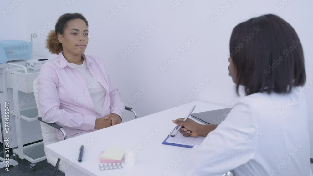 Female physician writing symptoms, talking to patient in clinic, diagnosis Female physician writing symptoms, talking to patient in clinic, diagnosis