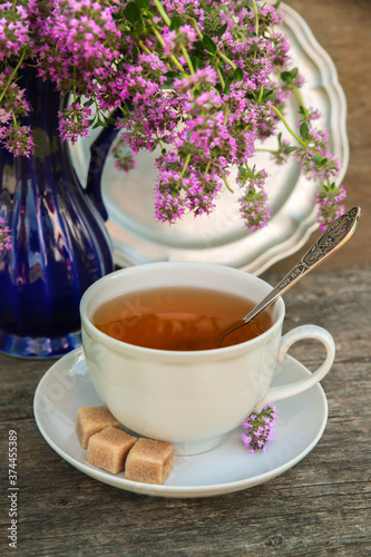 White cup of tea on thyme background on an old wooden table on a clear sunny day