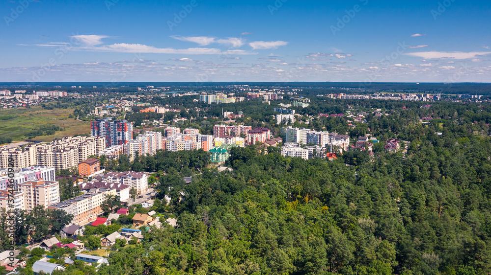 Aerial view photo of cityscape and skyline at summer sunny day. Urban buildings between green trees. Beautiful view of city downtown.