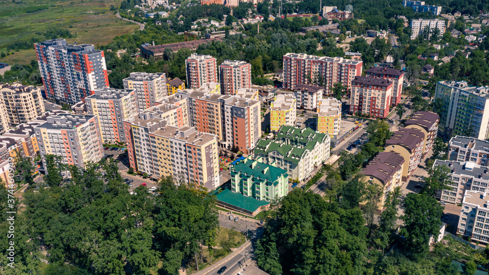 Beautiful photo from drone of city buildings between green trees. Aerial view shot of cityscape at summer sunny day.
