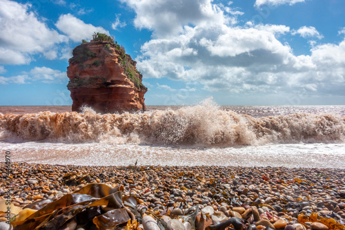 Waves roll onto the beach at Ladram Bay in South Devon, England. Sandstone cliffs have eroded over time to leave a free standing stack