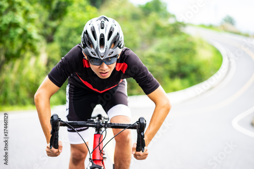 bicyclist man ridding bike going fast on mountain road, racing marathon event, race for charity, wearing cyclist gear and helmet protection, healthy fit athlete person staying active doing sports