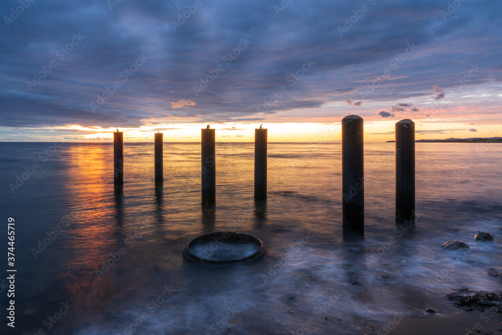 Long exposure sunset over beach with poles and dramatic sky colors in south Sweden. Selective focus.