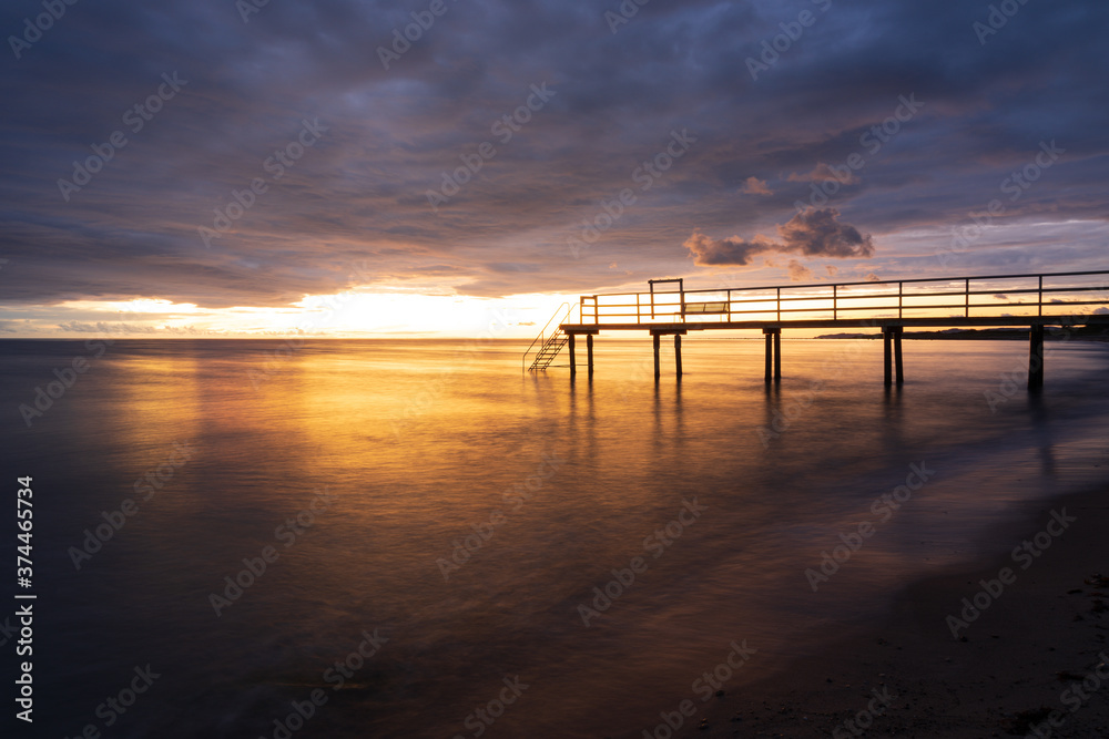 Bathing jetty with reflection in the sea during golden sunset in south Sweden. Selective focus.