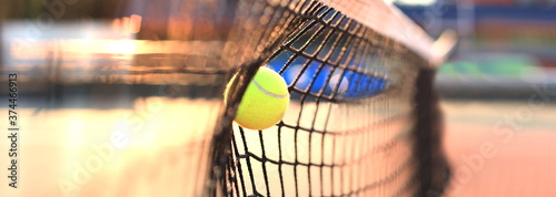Bright greenish yellow tennis ball hitting the net.