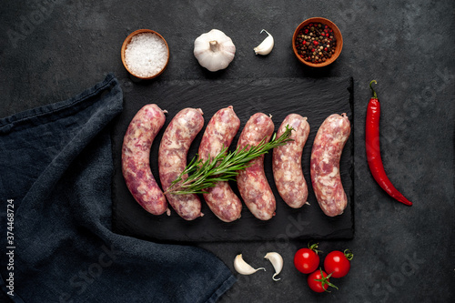 raw grilled sausages with spices on a slate board on a stone background
