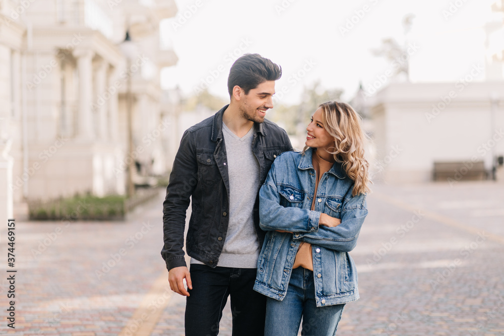Stylish man looking at girlfriend with love. Outdoor portrait of curly girl having fun at date.