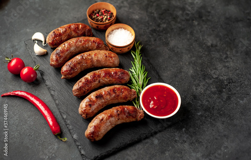 grilled sausages with spices on a slate board on a stone background with copy space for your text
