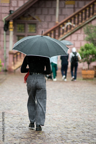 Portrait on back view of girl walking in the street with a black umbrella