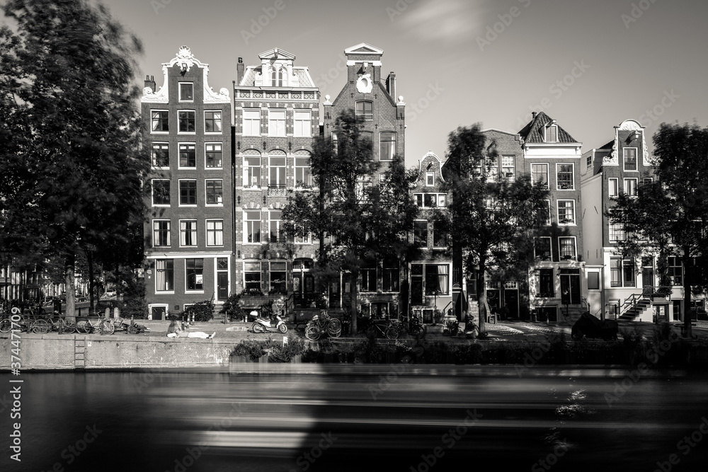 Obraz premium Amsterdam, Holland, the Netherlands - July 6 2020: capture of the typical Amsterdam scenery in black and white with canal, canalo house, clouds and the iconic buildings of the city