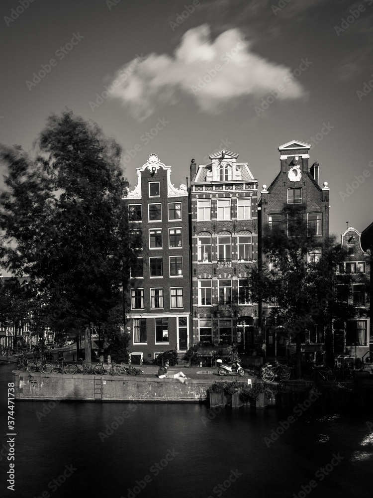 Amsterdam, Holland, the Netherlands - July 6 2020: capture of the typical Amsterdam scenery in black and white with canal, canalo house, clouds and the iconic buildings of the city